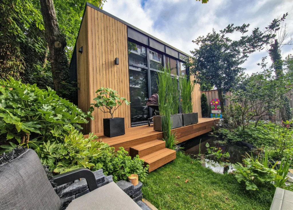 Garden Studio Vista surrounded by green grass and bushes, pond, wooden finish, large windows