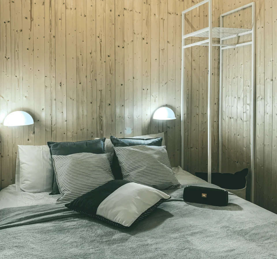 Bedroom in a Tiny House with a double bed, two lamps, a JBL speaker, and pillows.