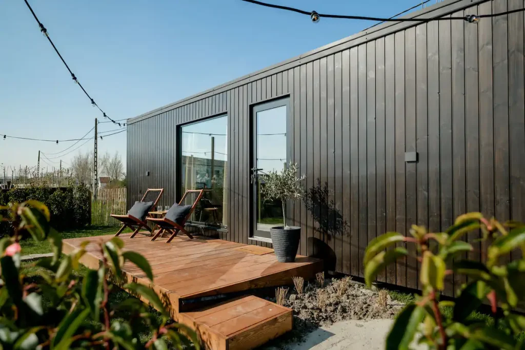 Prefab tiny house with a wooden terrace, ambient lighting, green plants